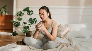 a woman practicing mindfulness, sitting on her bed with a cup of tea.