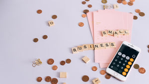 Scrabble tiles spell out "small business" and are surrounded by an iPhone calculator, coins, and pink notepad – all encouraging the viewer to support small business 