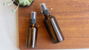 amber glass spray bottles against a wood table and a succulent set the scene for a DIY room spray with essential oils