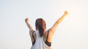 a woman in an athletic tank top raises her hands to the sky – she looks confident and happy. 