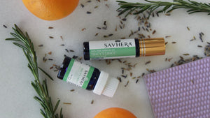 a bottle and roller of Tracy's Grace: Savhera's calming essential oil blend. Surrounded by fresh oranges, rosemary sprigs, and dried lavender.